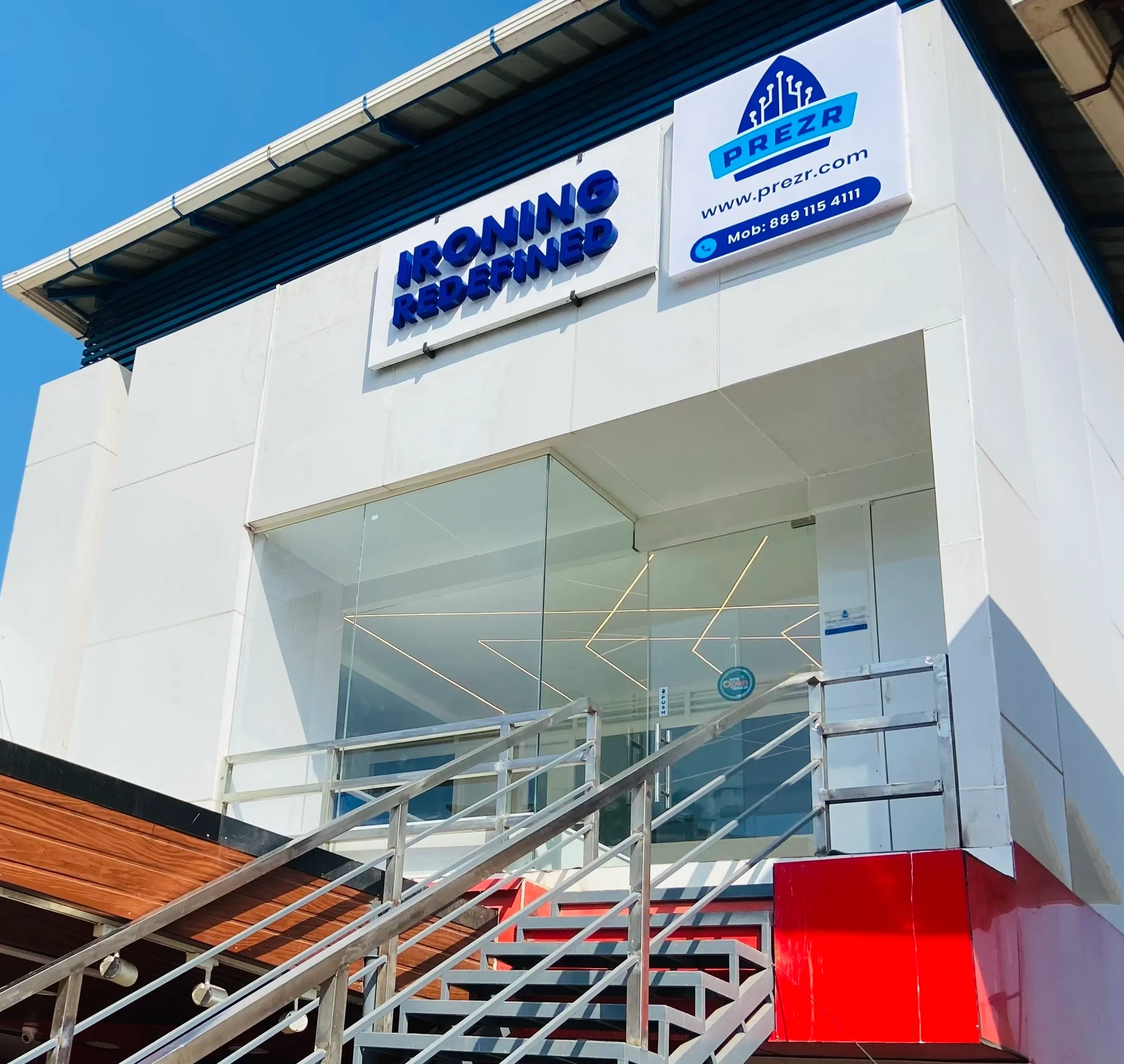 The Prezr building on Cotton Hill Road: a white corner unit with a glass front and a metal stair up to the first floor. The signs read Ironing Redefined and Prezr.